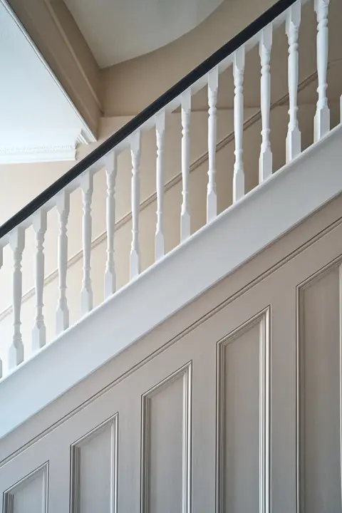 Close-up of white spindles and a dark handrail above pink stair panelling