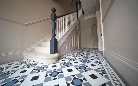 Foot of the staircase with a dark newel post and handrail, white spindles and a geometric tiled floor
