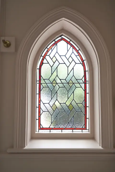 Gothic arched stained glass window set in a light pink wall with a painted surround