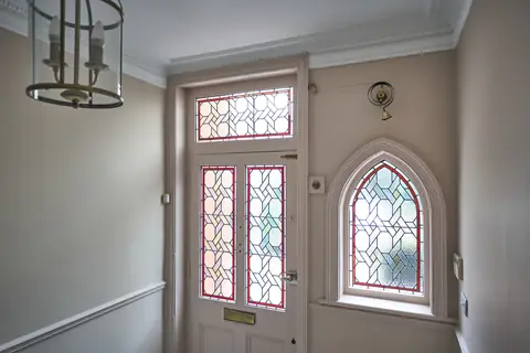 Stained glass front door and arched window with pink walls, a white cornice, lantern and brass bell