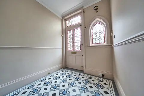 Entrance hall with pink walls, a front door painted to match and an arched stained glass window